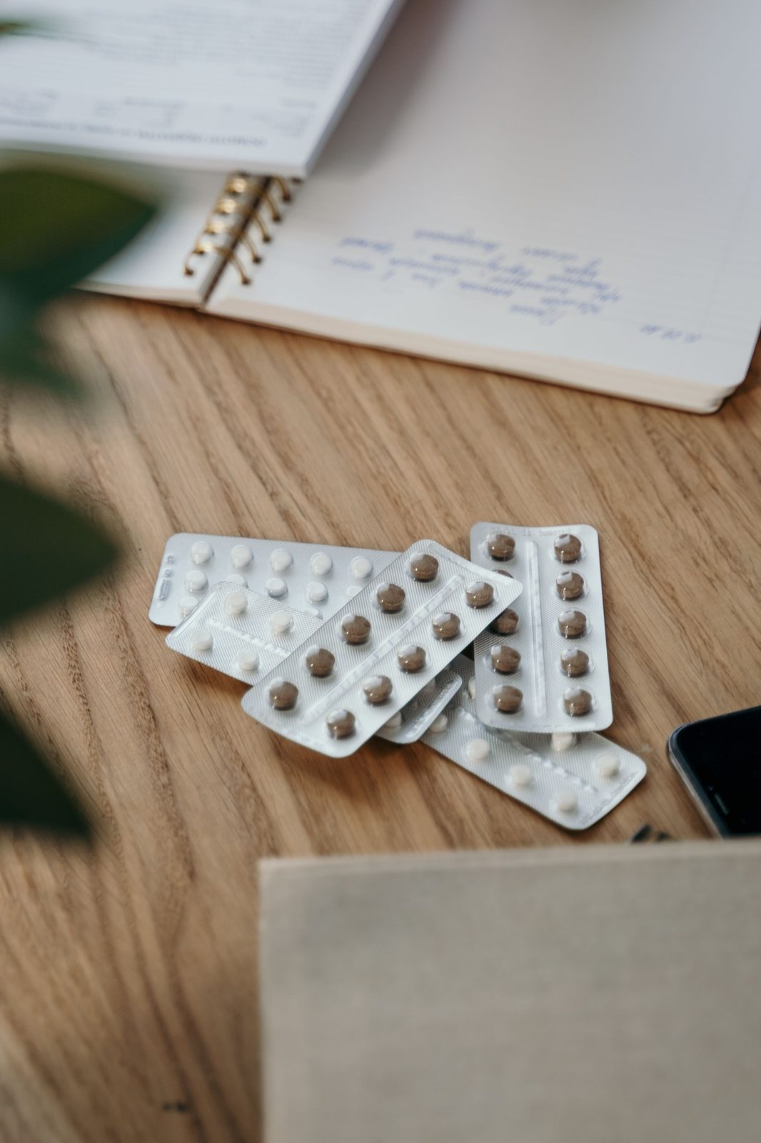 Blister packs of medication beside an open notebook on a wooden table